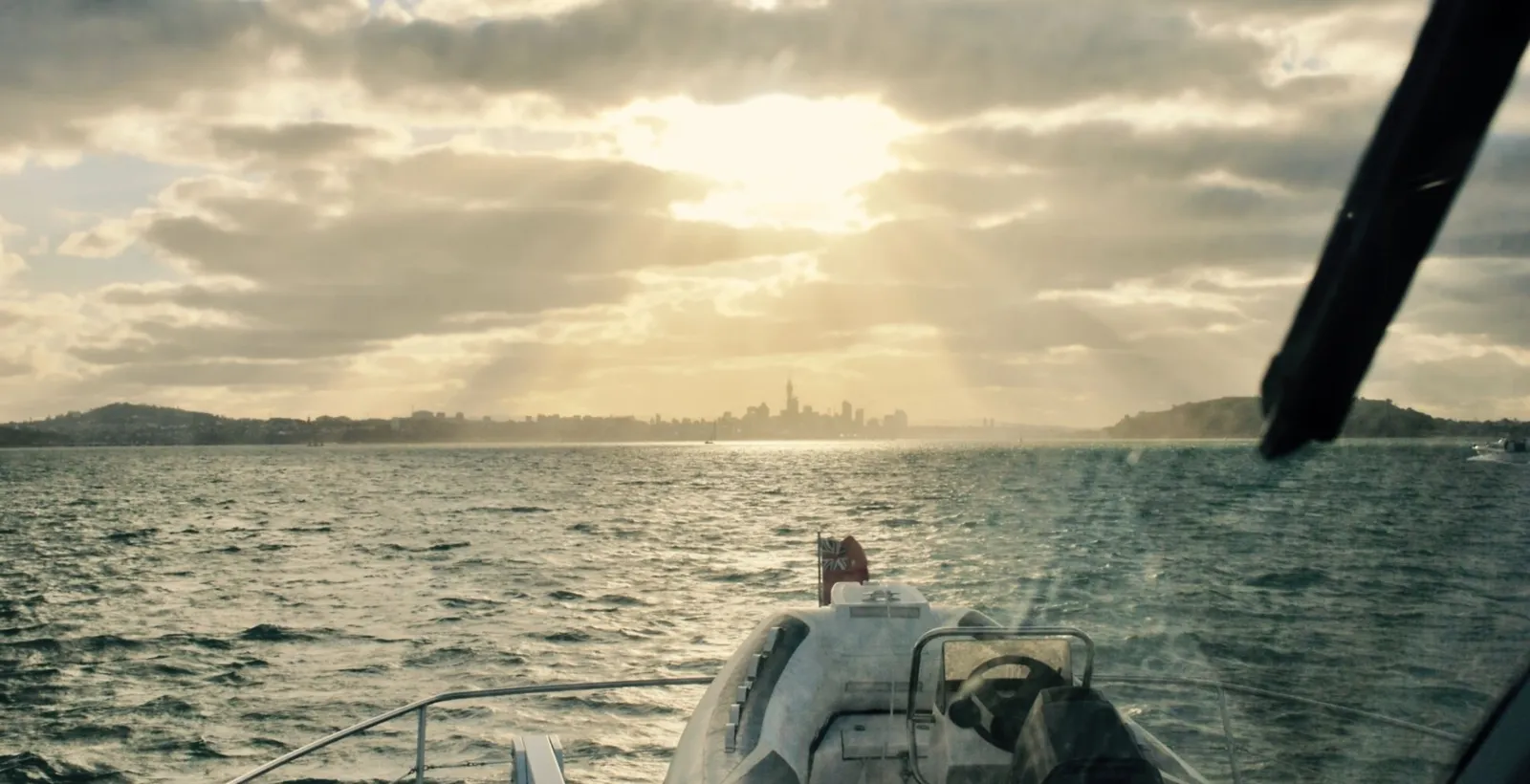 Sun rays breaking through cloud over the harbour, seen from the bow of a boat heading for the city