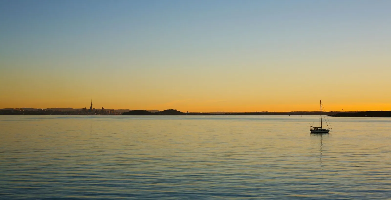 A lone yacht at anchor on a calm, golden harbour at sunset