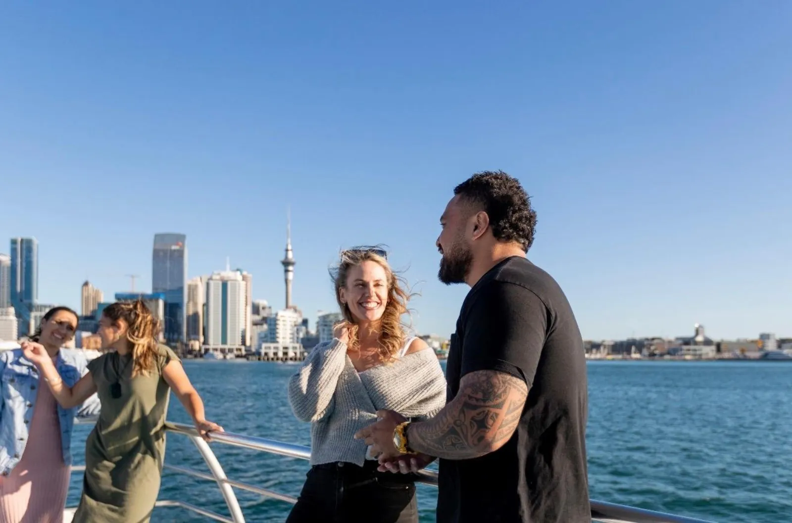 Passengers chatting at the deck rail with the Auckland skyline behind