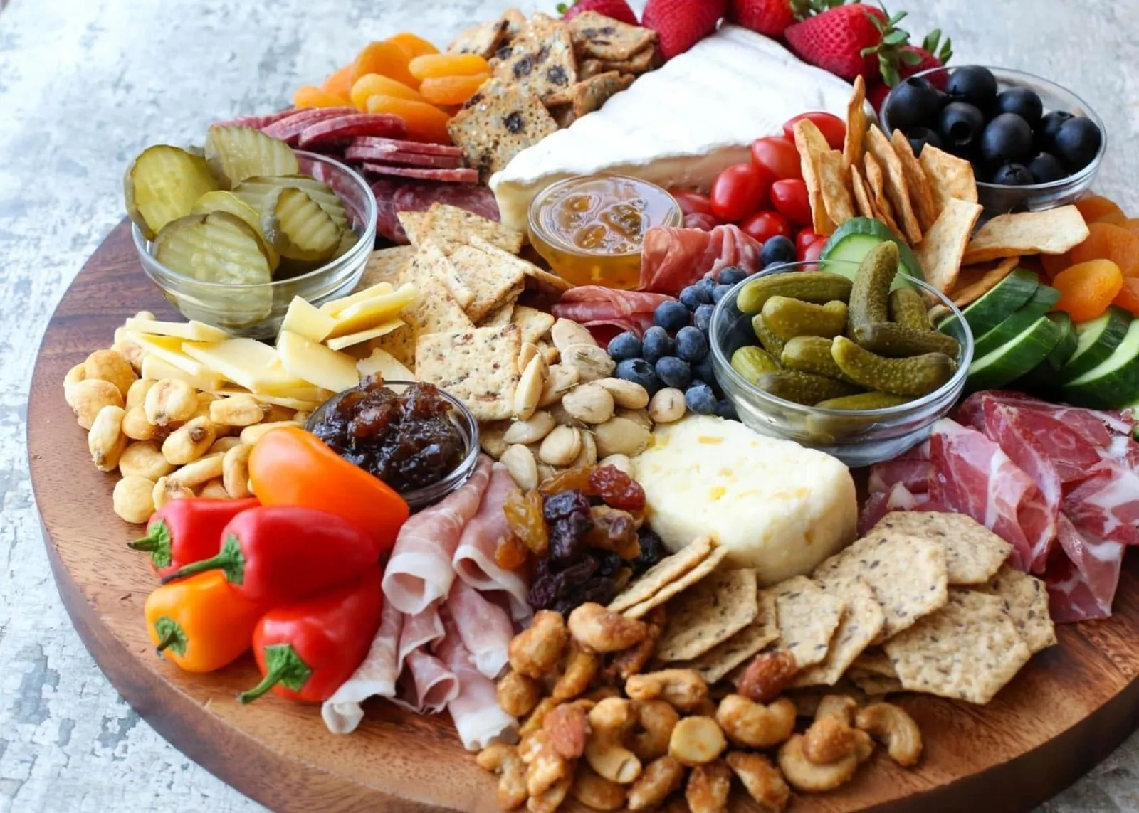 Round board of cheeses, cured meats, crackers, nuts, pickles and fruit