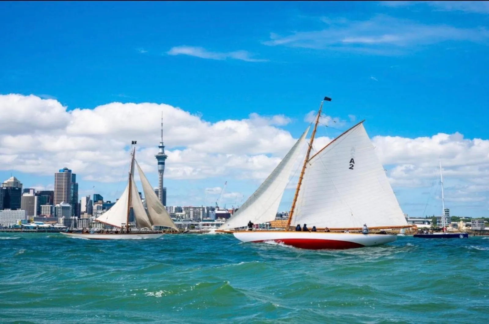 Two classic gaff-rigged yachts sailing past the Auckland skyline