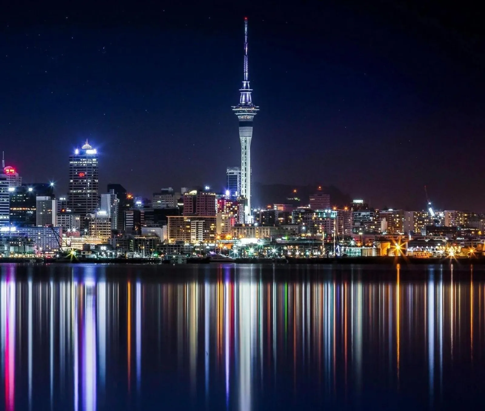 Sky Tower and city lights reflected in long colourful streaks across the harbour