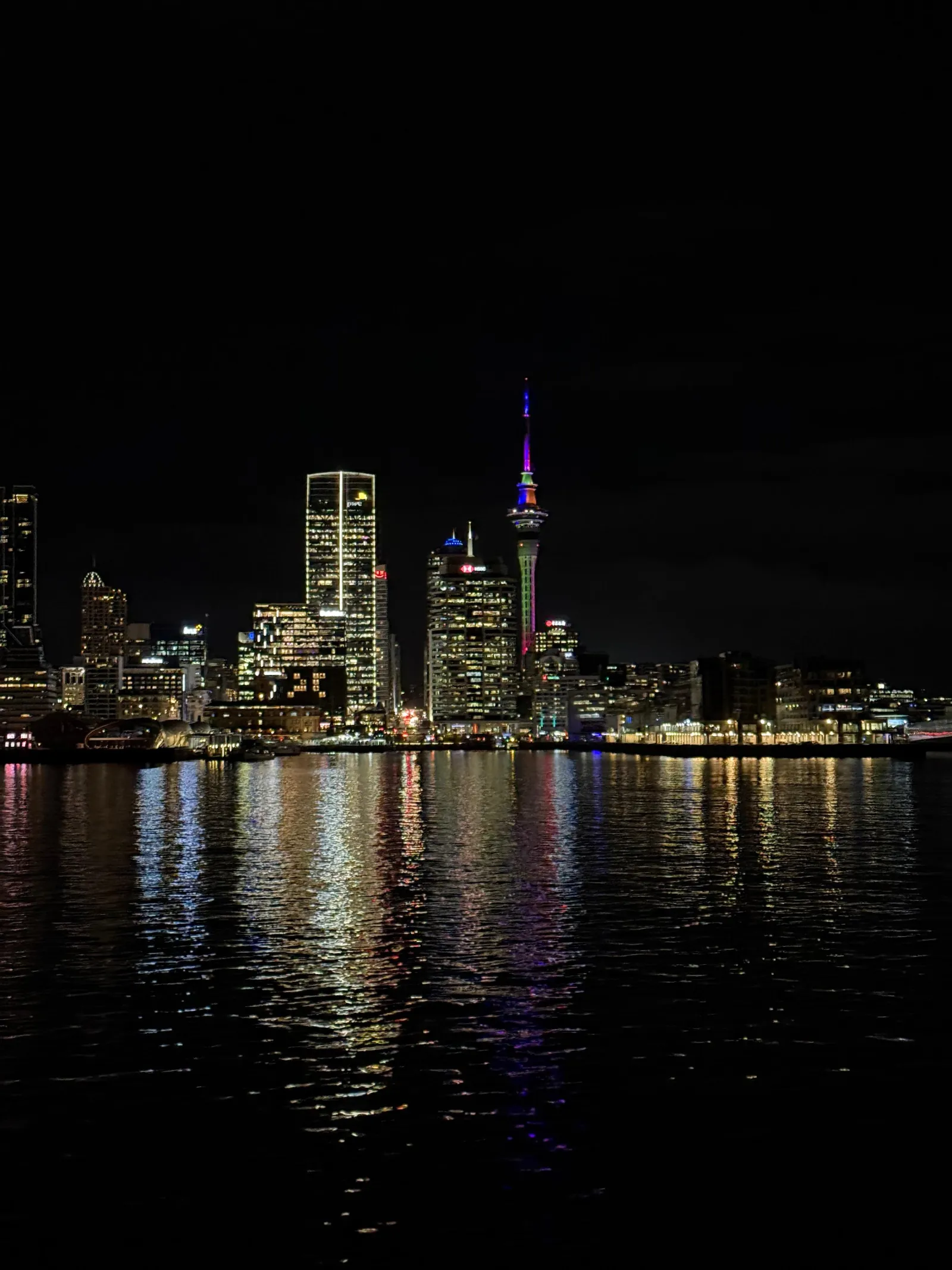 Sky Tower glowing purple above the dark city skyline and harbour at night