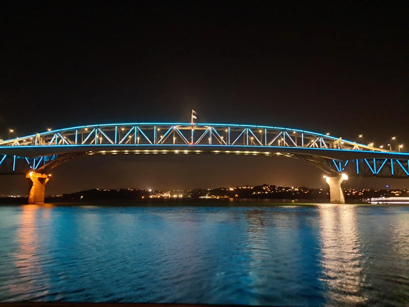 Auckland Harbour Bridge lit in blue at night over calm reflective water