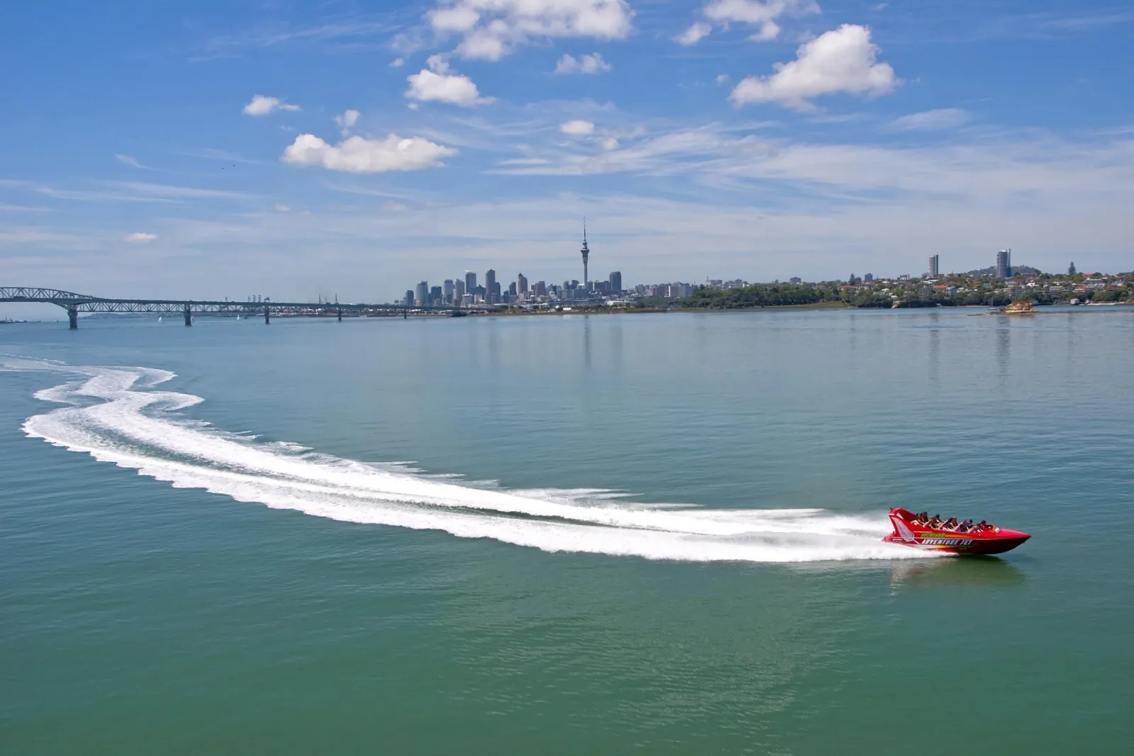 Jet boat carving a white wake with the Harbour Bridge and Sky Tower behind