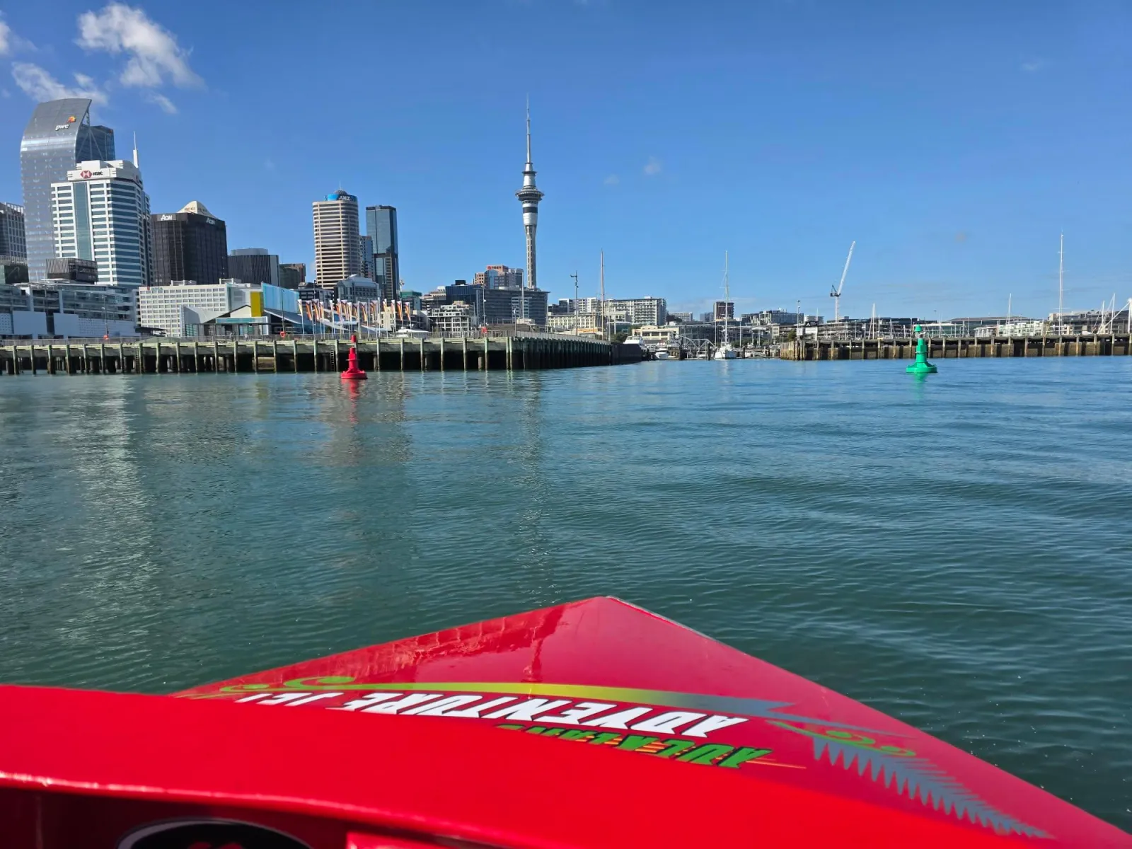 Bow of the red jet boat facing the Auckland waterfront and Sky Tower