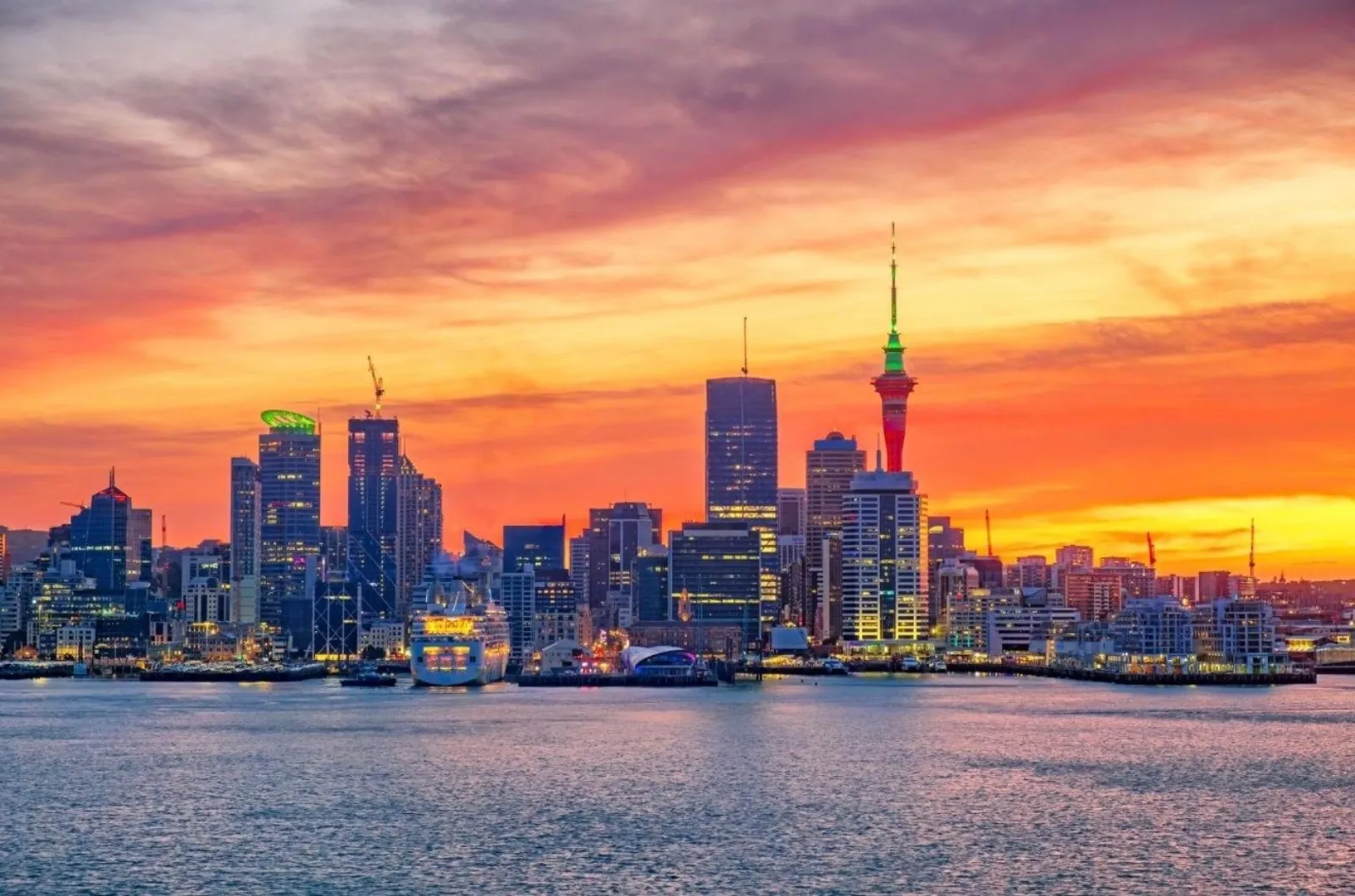 Auckland city skyline lit up against a vivid red and purple sunset over the harbour