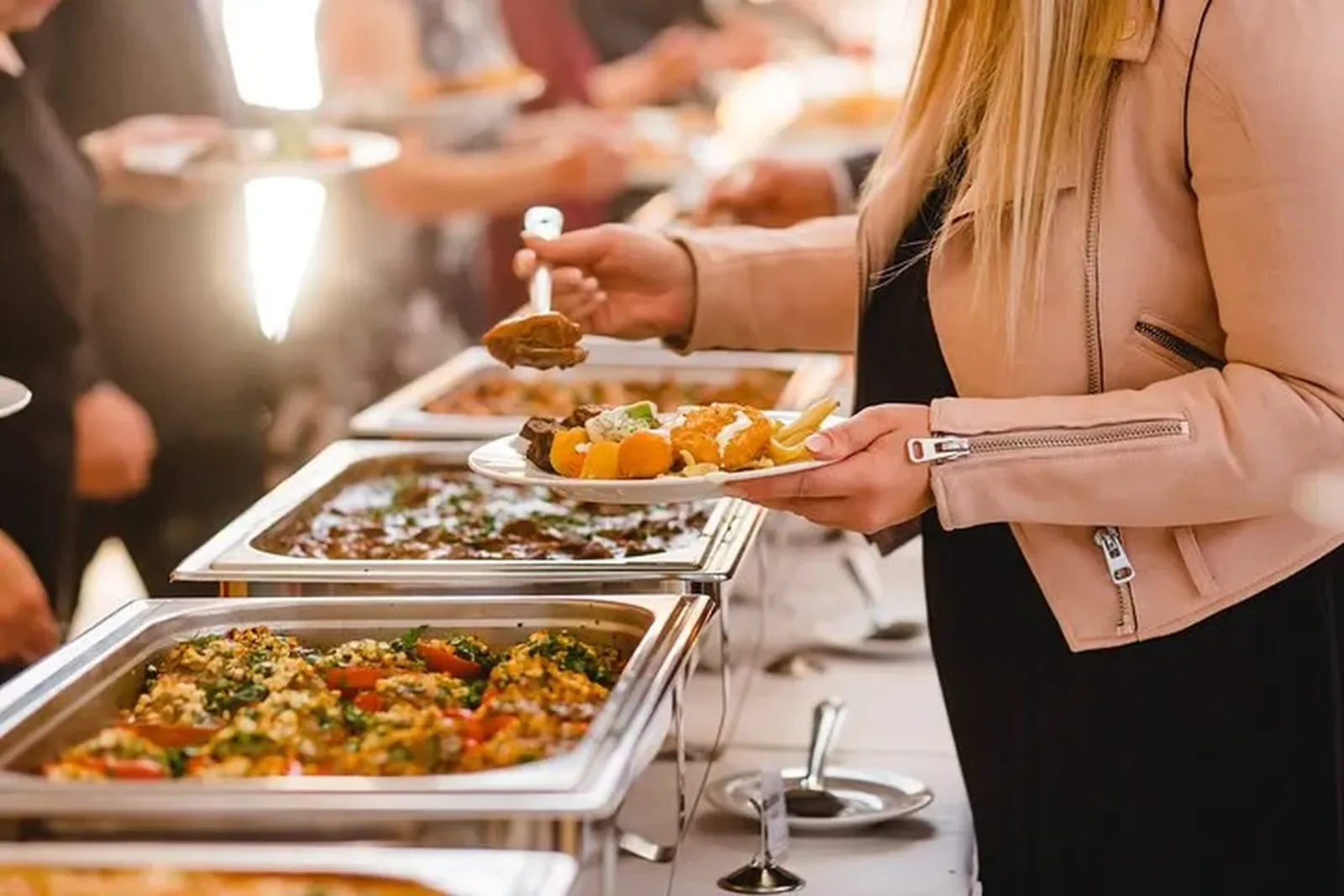 Guest serving roast vegetables onto a plate from a row of buffet warming trays