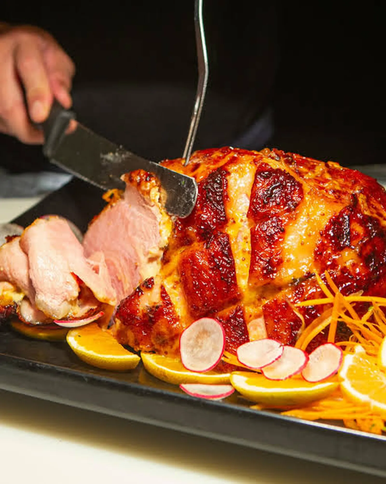 Glazed roast ham being carved, garnished with orange slices and sliced radish