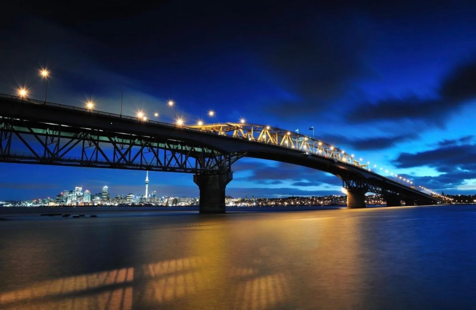 Auckland Harbour Bridge lit up at night with the Sky Tower in the distance