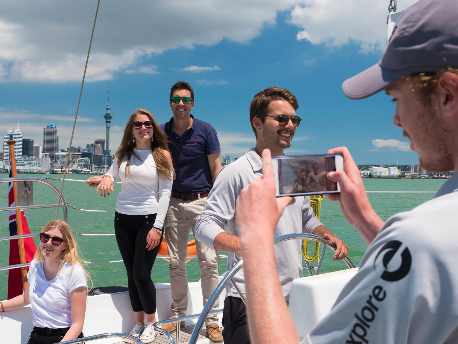 Crew member photographing guests on deck with the Sky Tower in the background