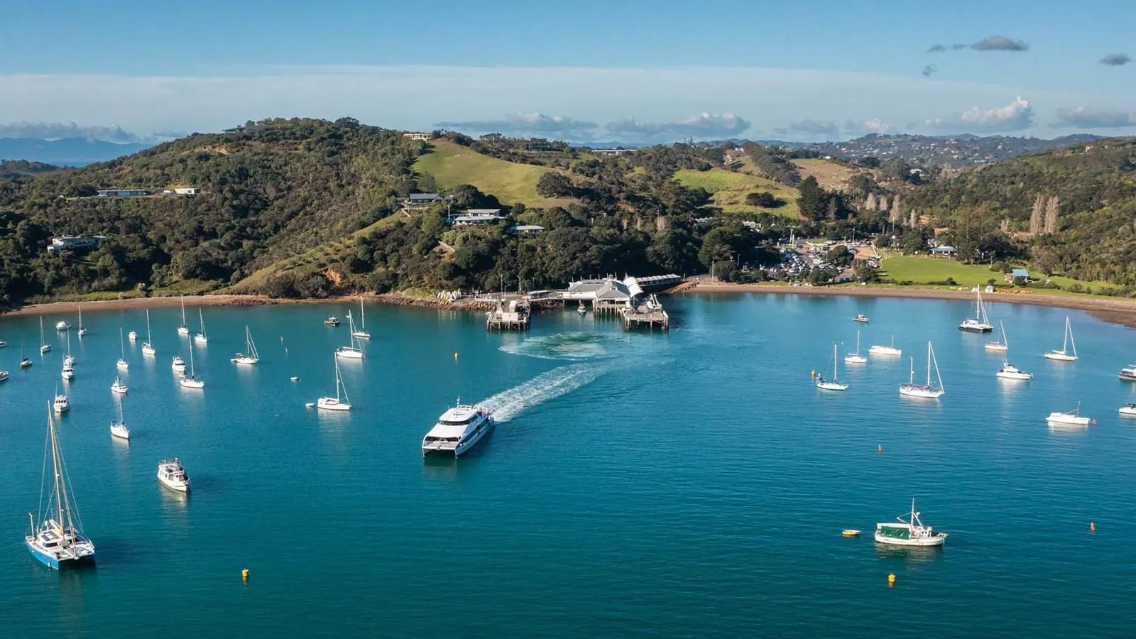 Aerial view of a fast ferry crossing a Waiheke bay among moored yachts