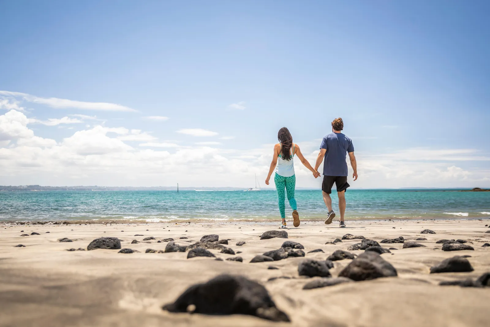 Couple walking hand in hand toward the sea across a rocky beach