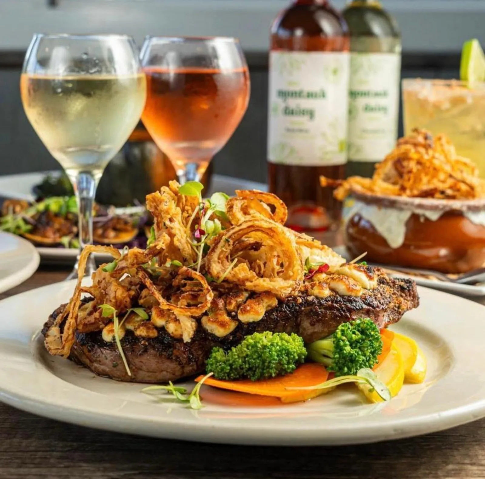 Steak topped with crispy onions beside glasses of wine at the tavern