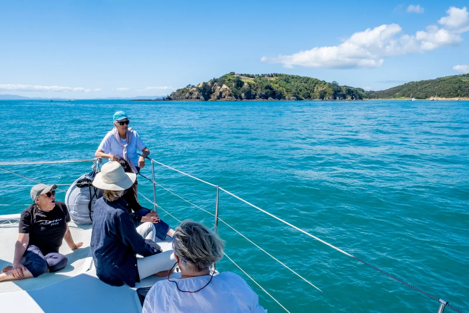 Guests sitting on the bow as the catamaran nears a green island