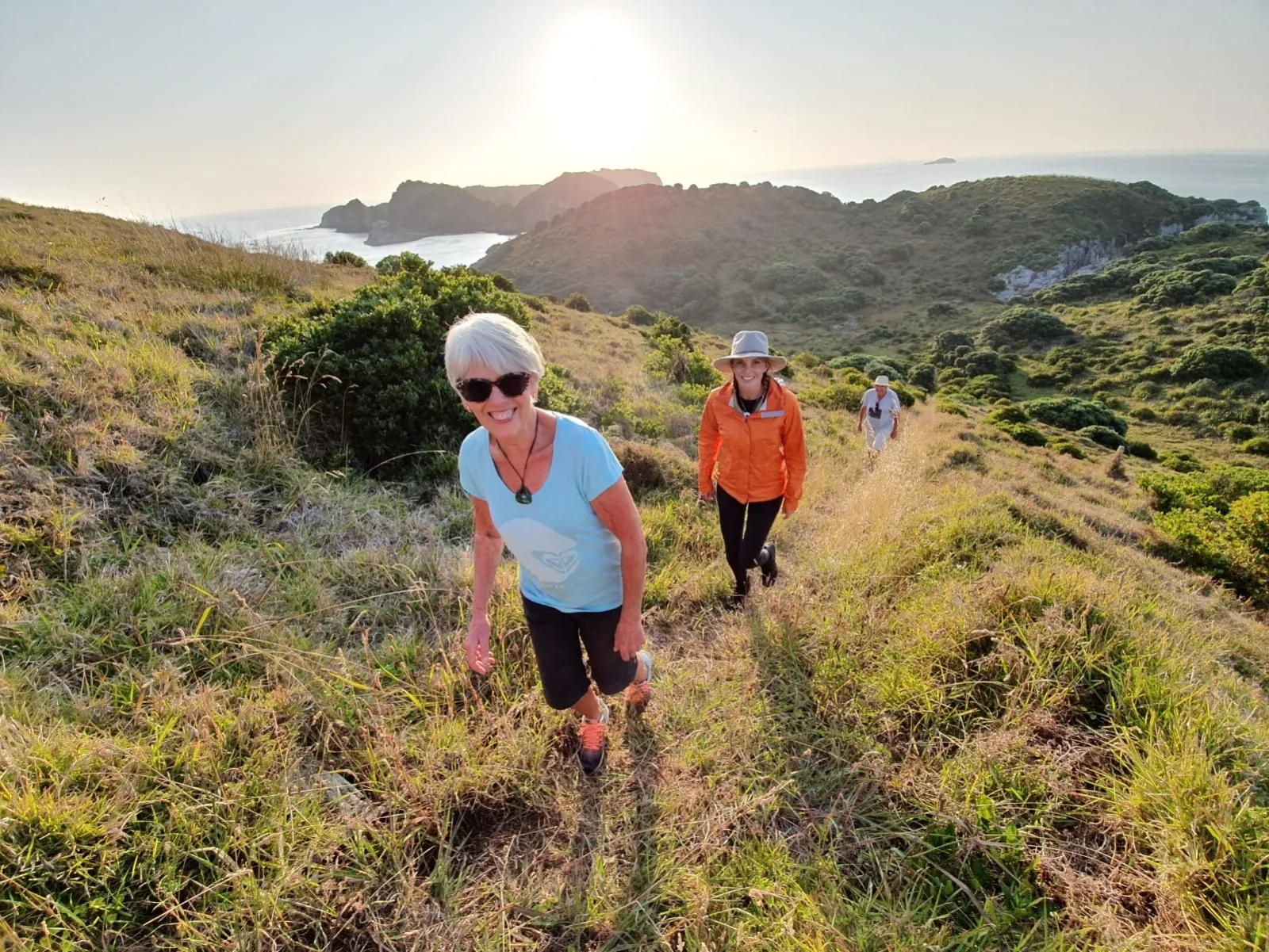 Smiling walkers on a grassy island ridge above the sea