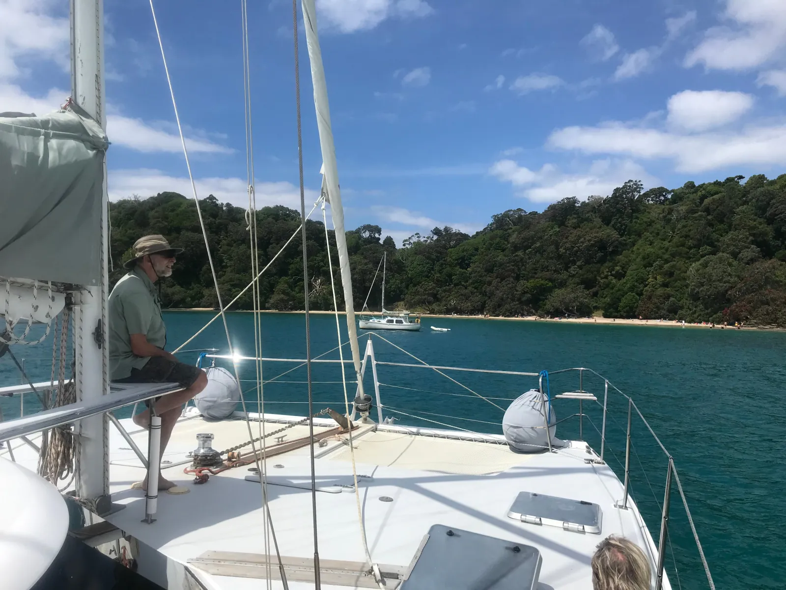 Skipper seated on deck in a sheltered bay with a sandy beach