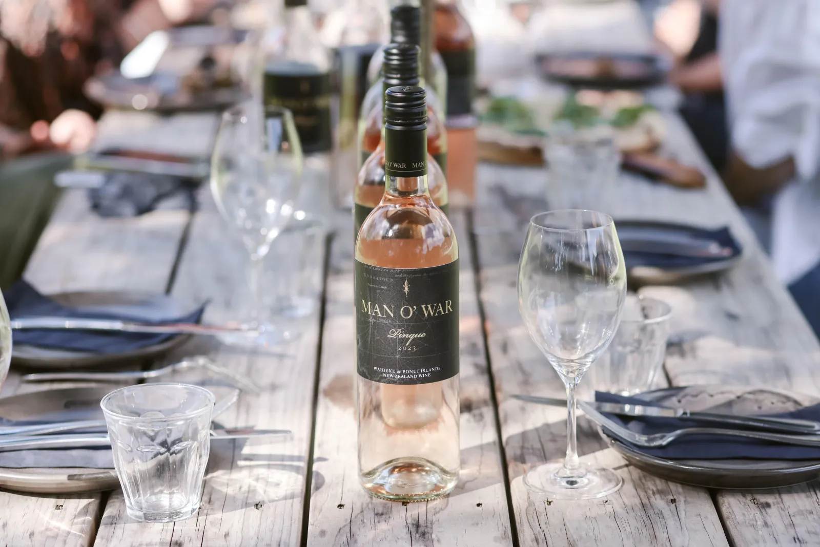 Long outdoor table set with glasses and a bottle of Man O' War rosé